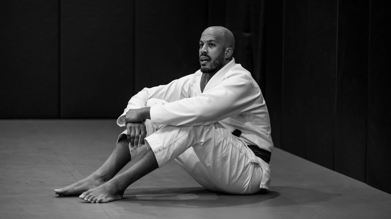 Ryan sitting on the mat in a jiu-jitsu gi, mid-conversation